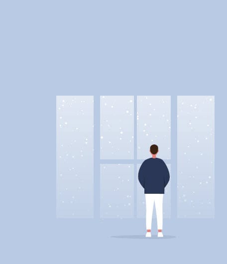 Local-831 A person stands indoors, facing large windows and looking out at falling snow.